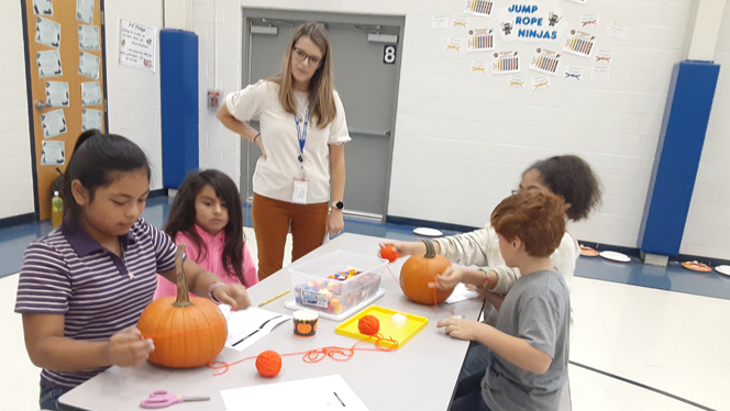 Students crafting with pumpkins at a table. Students crafting with pumpkins at a table.
