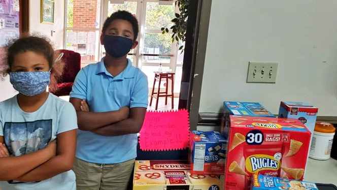 Children standing with arms folded next to boxes of food